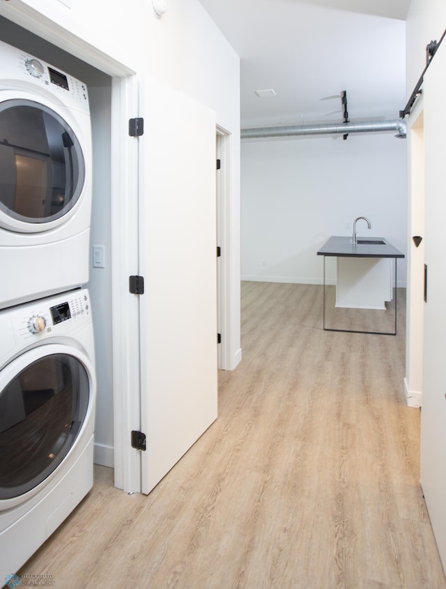 laundry room with light hardwood / wood-style floors, a barn door, stacked washing maching and dryer, and sink