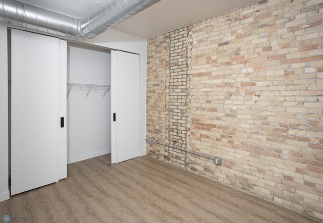 unfurnished bedroom featuring a closet, brick wall, and light hardwood / wood-style flooring