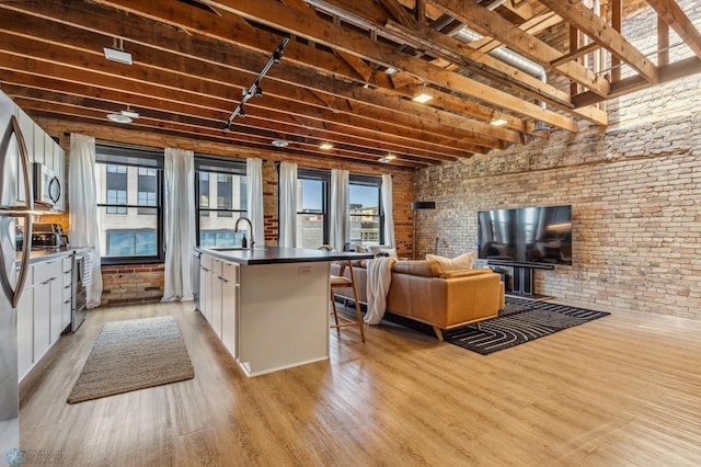 kitchen with white cabinetry, stainless steel appliances, brick wall, light hardwood / wood-style floors, and a center island with sink