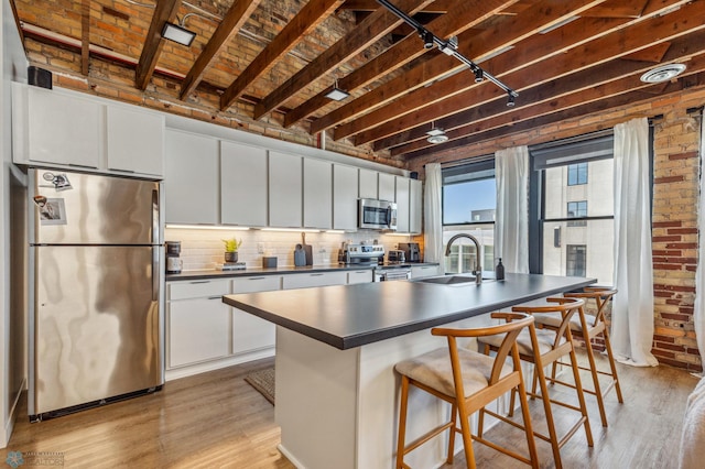 kitchen with white cabinets, sink, stainless steel appliances, and brick wall