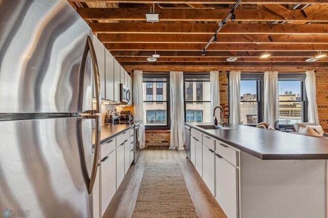 kitchen featuring sink, stainless steel appliances, an island with sink, white cabinets, and light wood-type flooring