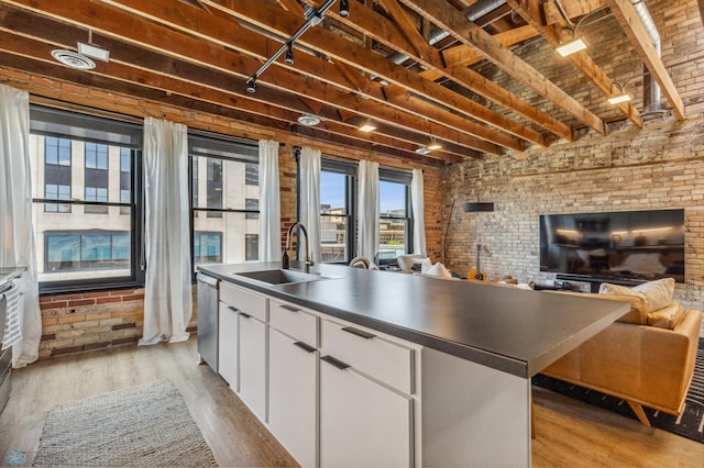 kitchen featuring brick wall, light wood-type flooring, white cabinetry, and sink