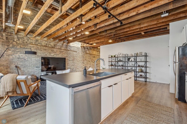 kitchen with a kitchen island with sink, white cabinets, sink, stainless steel appliances, and brick wall