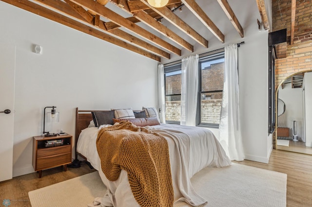 bedroom featuring hardwood / wood-style floors, beam ceiling, and brick wall