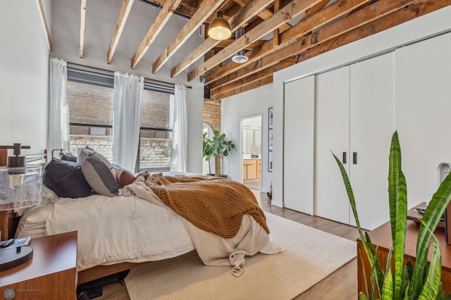 bedroom with beamed ceiling, ensuite bathroom, and light hardwood / wood-style flooring