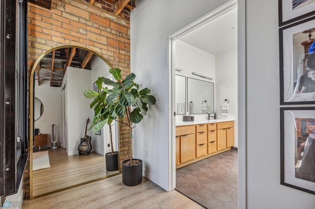 hallway featuring light hardwood / wood-style flooring, brick wall, and sink