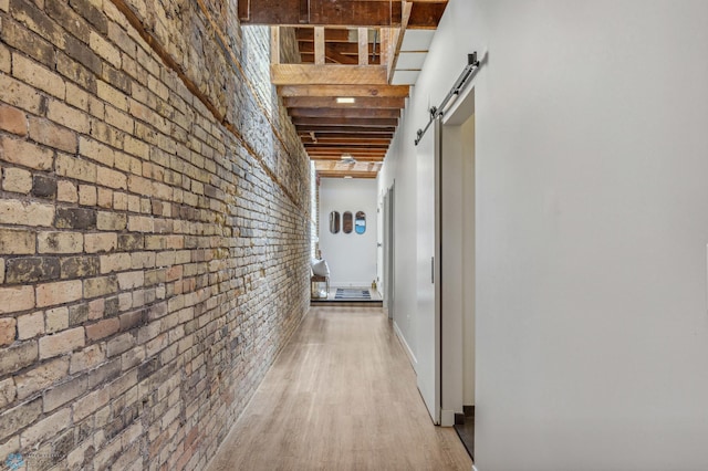 corridor featuring a barn door, light wood-type flooring, and brick wall