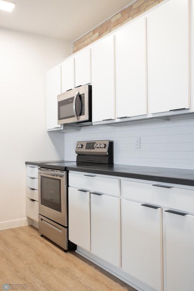 kitchen with backsplash, stainless steel appliances, white cabinetry, and light hardwood / wood-style flooring