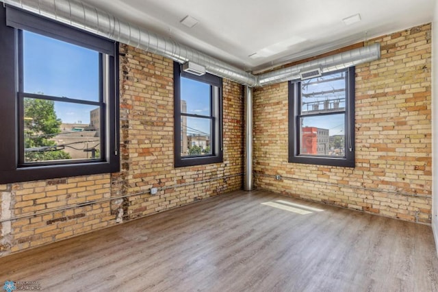 unfurnished room with hardwood / wood-style floors, plenty of natural light, and brick wall