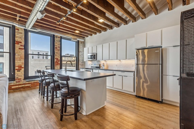 kitchen featuring white cabinets, a kitchen breakfast bar, an island with sink, appliances with stainless steel finishes, and brick wall