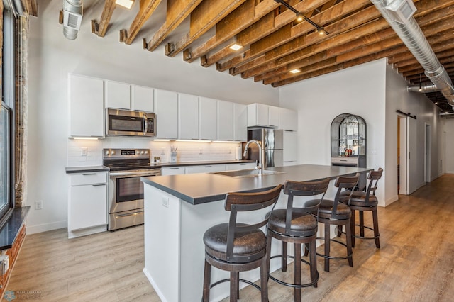 kitchen featuring white cabinets, an island with sink, light hardwood / wood-style floors, and appliances with stainless steel finishes