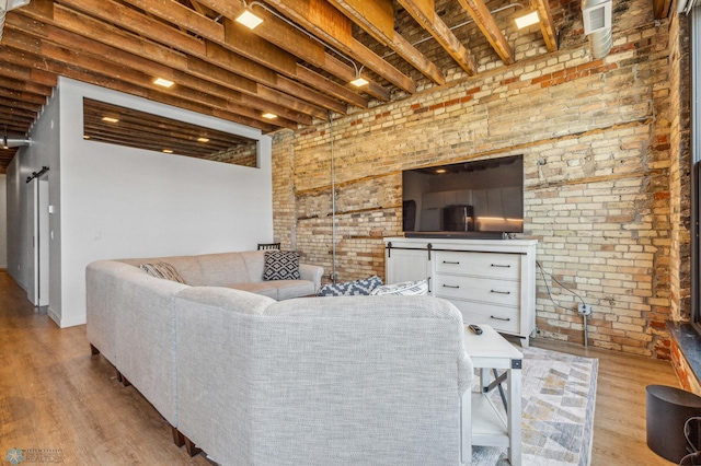 living room featuring beamed ceiling, brick wall, and light wood-type flooring