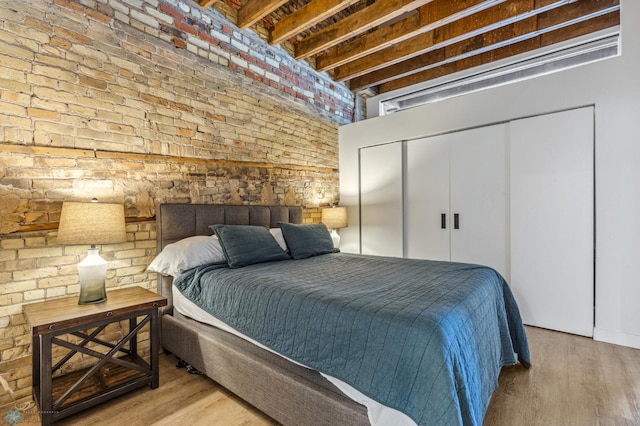 bedroom with beamed ceiling, light hardwood / wood-style floors, brick wall, and a closet