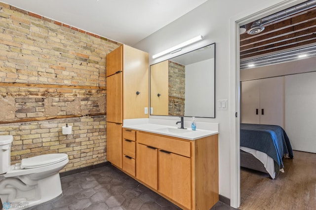 bathroom with hardwood / wood-style floors, vanity, brick wall, and toilet