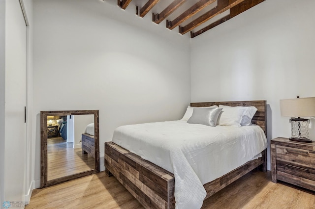 bedroom with vaulted ceiling with beams and light wood-type flooring