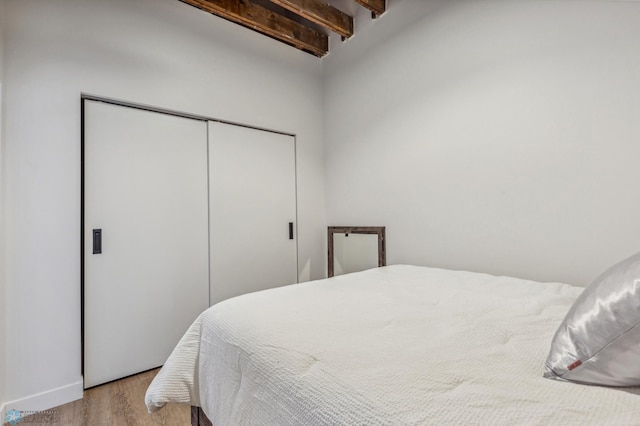 bedroom featuring vaulted ceiling with beams, light hardwood / wood-style floors, and a closet