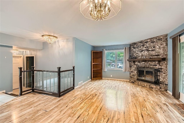 unfurnished living room with an inviting chandelier, a fireplace, and light hardwood / wood-style floors