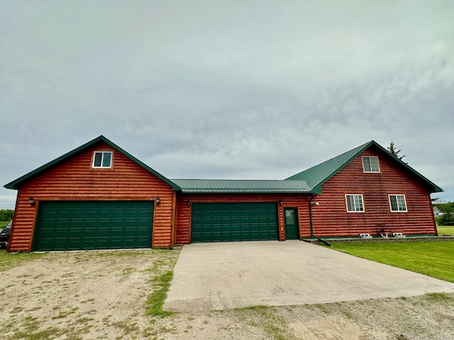 log-style house with driveway, metal roof, log veneer siding, and a garage