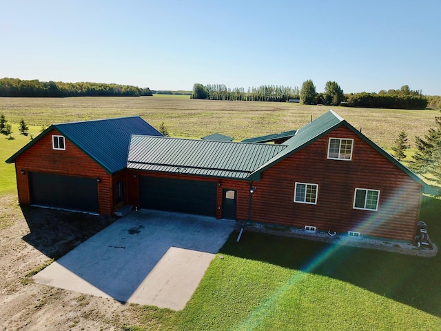 view of front of property featuring a front lawn, driveway, a rural view, and a garage
