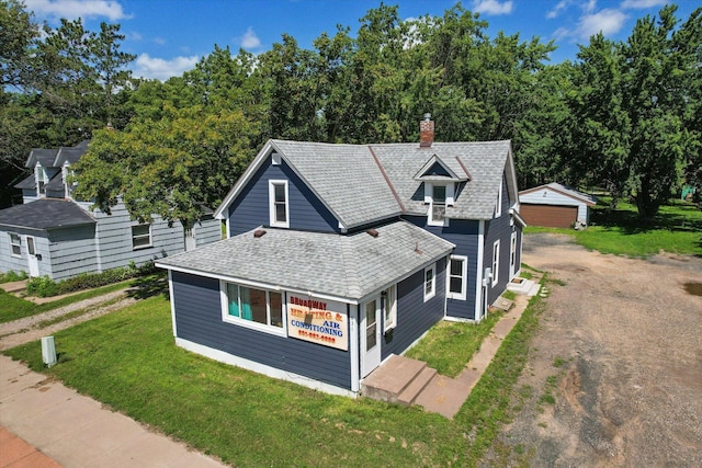 view of front of home featuring driveway, a chimney, roof with shingles, an outdoor structure, and a front lawn