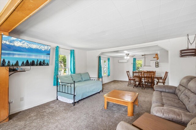 carpeted living room featuring a ceiling fan, an AC wall unit, a healthy amount of sunlight, and baseboards