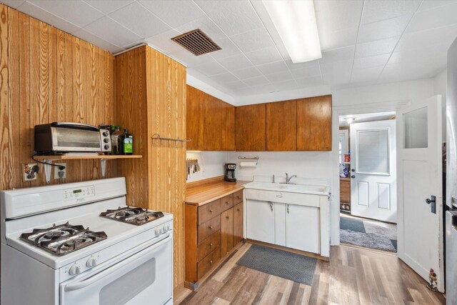 kitchen with white range with gas stovetop, visible vents, light wood-style flooring, brown cabinets, and light countertops