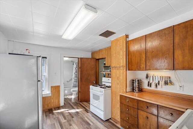 kitchen featuring white range with gas stovetop, light wood-style flooring, brown cabinets, freestanding refrigerator, and light countertops