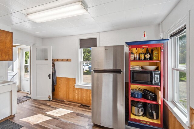 kitchen with a wealth of natural light, freestanding refrigerator, black microwave, and a wainscoted wall