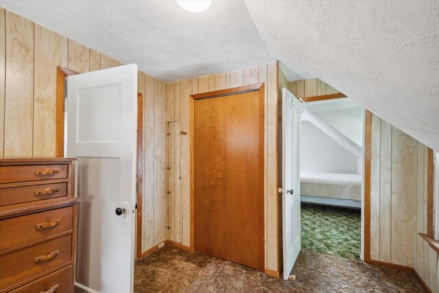 hallway with a textured ceiling, wood walls, and lofted ceiling