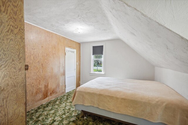 carpeted bedroom featuring a textured ceiling, wood walls, and vaulted ceiling