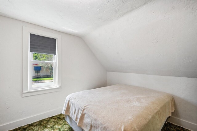 bedroom with lofted ceiling, baseboards, a textured ceiling, and a textured wall