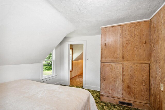 bedroom with lofted ceiling, visible vents, dark carpet, and a textured ceiling