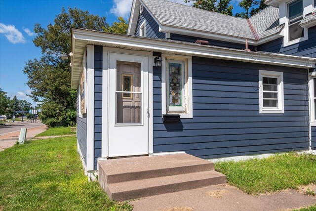 doorway to property with roof with shingles and a yard