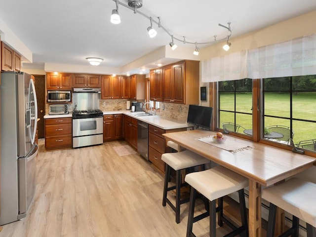 kitchen with tasteful backsplash, appliances with stainless steel finishes, sink, and light hardwood / wood-style flooring