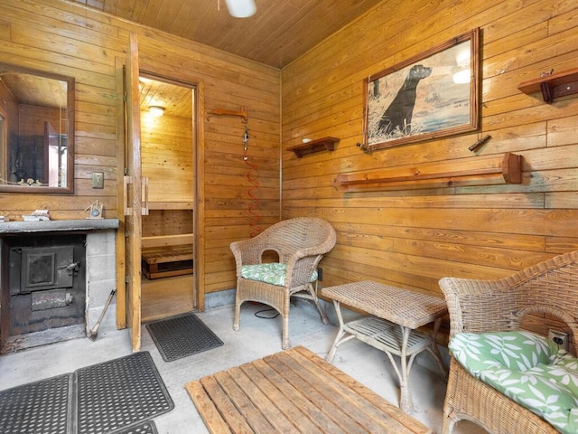 sitting room featuring wooden walls, wooden ceiling, concrete floors, and a wood stove