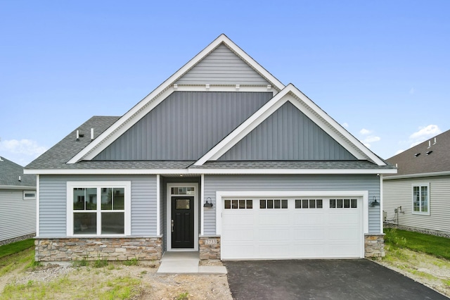 view of front of property with stone siding, driveway, a shingled roof, and board and batten siding