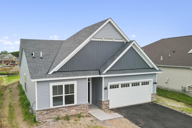 view of front of house featuring driveway, an attached garage, stone siding, and roof with shingles