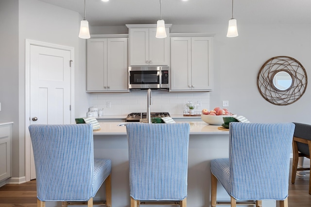 kitchen featuring tasteful backsplash, stainless steel microwave, light countertops, and decorative light fixtures