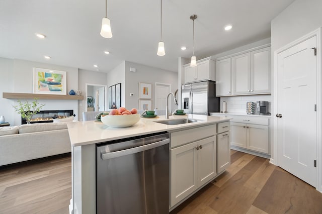 kitchen featuring open floor plan, light wood-type flooring, a glass covered fireplace, stainless steel appliances, and a sink