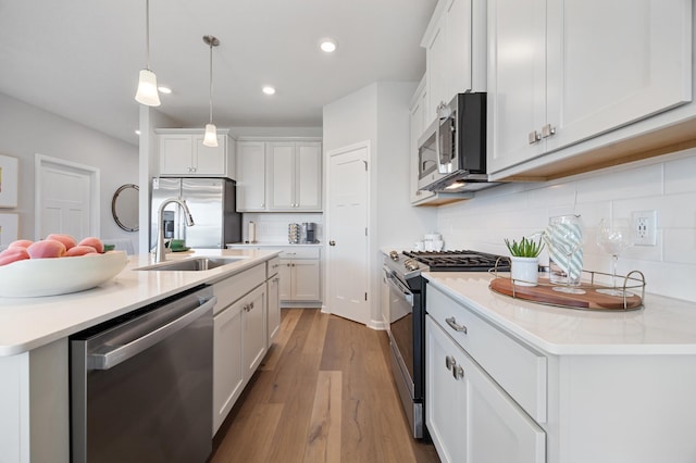 kitchen featuring a sink, decorative light fixtures, wood finished floors, stainless steel appliances, and white cabinets