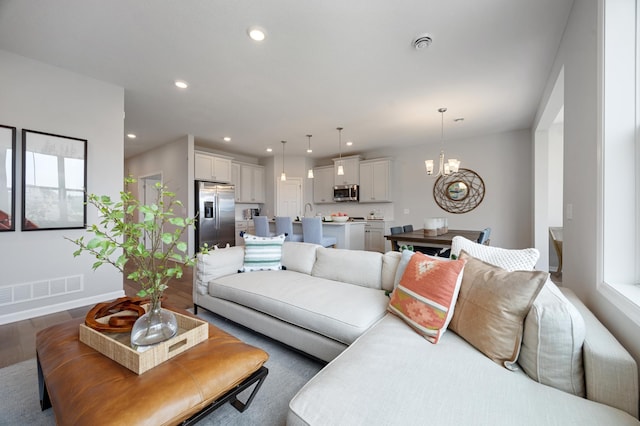 living room featuring visible vents, baseboards, recessed lighting, an inviting chandelier, and wood finished floors