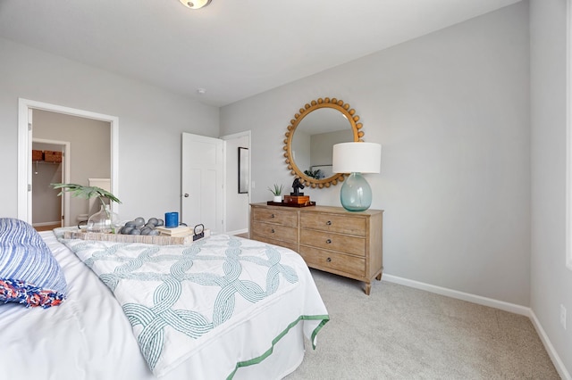 bedroom with a spacious closet, light colored carpet, and baseboards