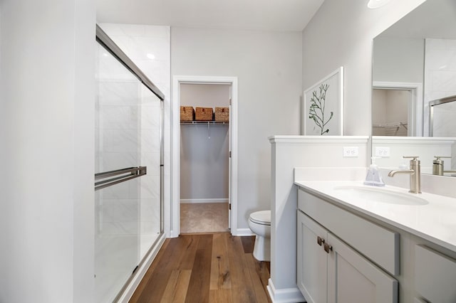 bathroom with a shower stall, a walk in closet, toilet, wood finished floors, and vanity