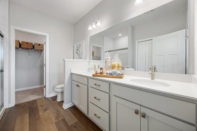 bathroom featuring hardwood / wood-style floors, dual bowl vanity, a shower with shower door, and toilet