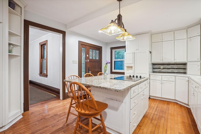 kitchen featuring decorative light fixtures, white cabinets, a kitchen bar, a center island, and light stone counters