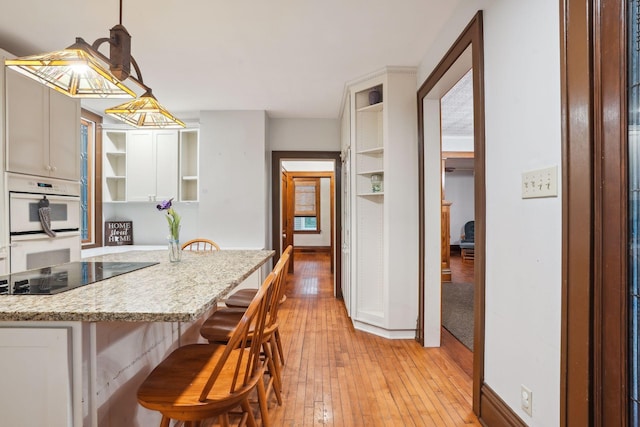 kitchen with pendant lighting, a breakfast bar, light stone counters, black electric stovetop, and light hardwood / wood-style floors