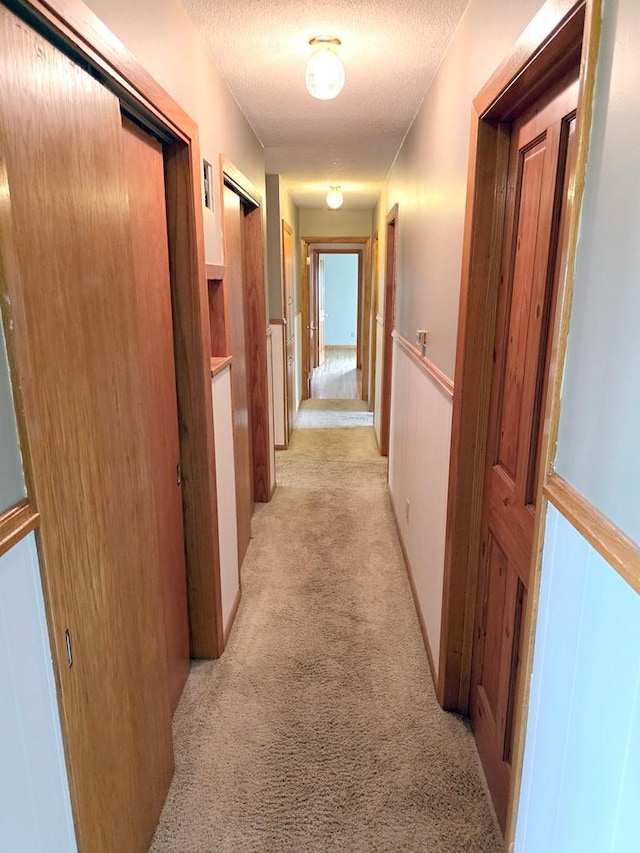 corridor with a textured ceiling and light colored carpet