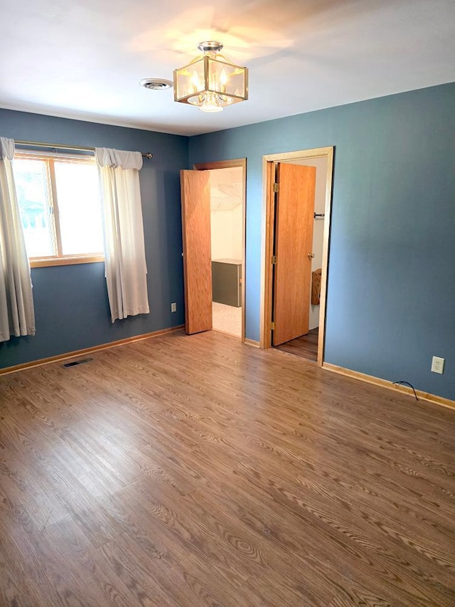 unfurnished bedroom featuring wood-type flooring, a walk in closet, an inviting chandelier, and a closet