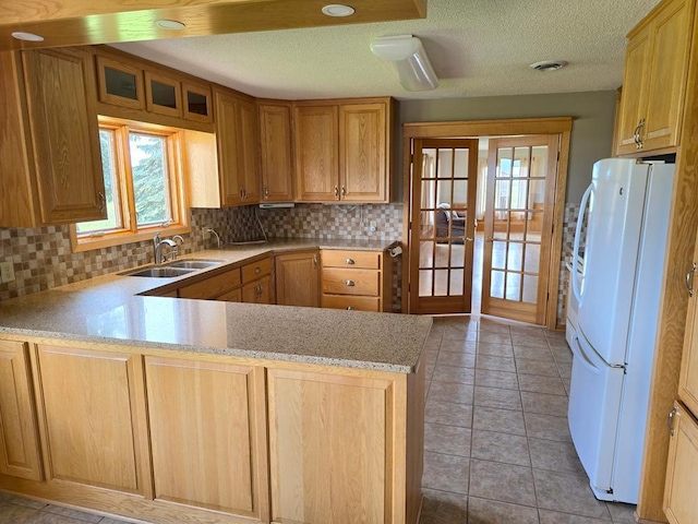 kitchen with kitchen peninsula, backsplash, white fridge, and sink