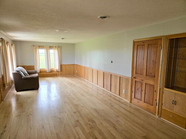 unfurnished room featuring a textured ceiling, light hardwood / wood-style flooring, and wood walls